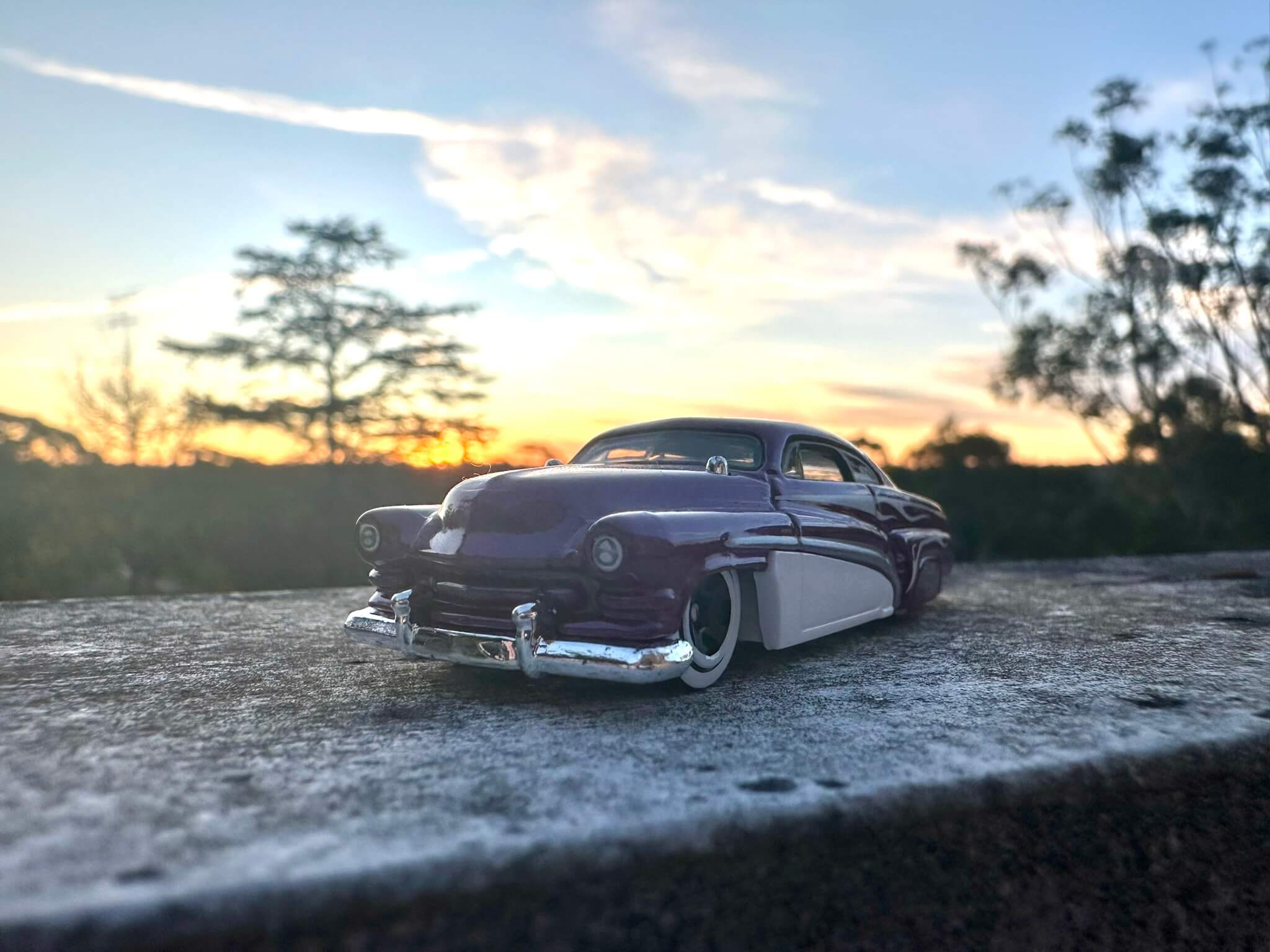 Purple hot wheels car perched on a railing with a sunset behind