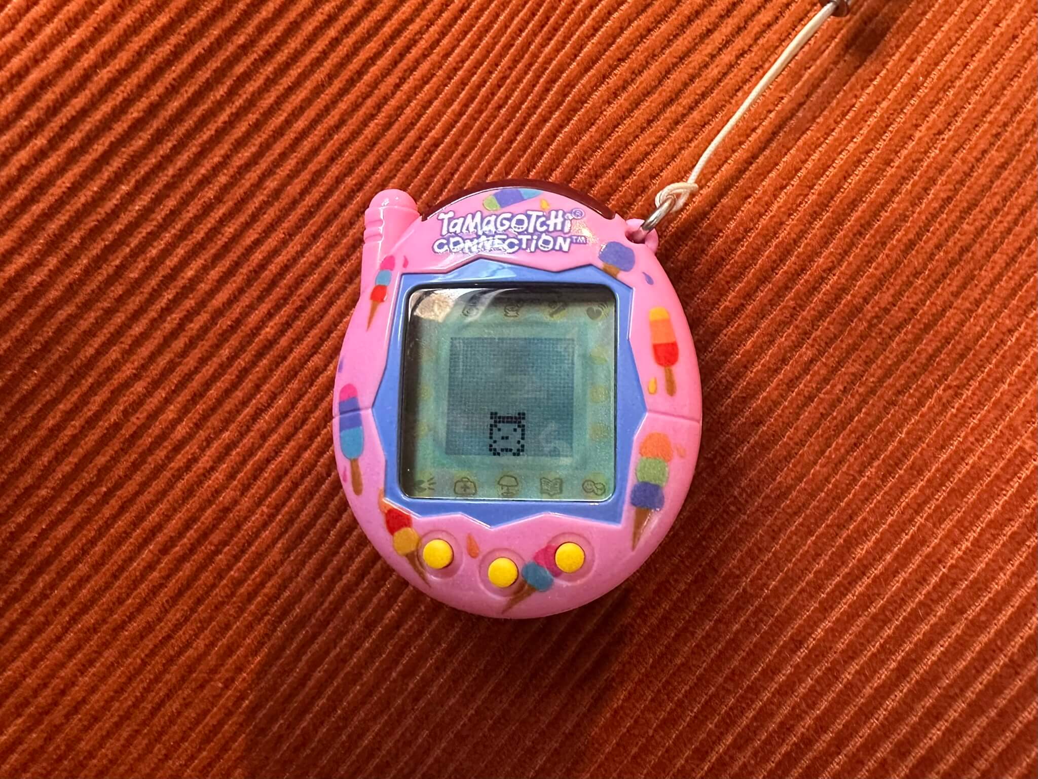 Pink tamagotchi on an orange corduroy fabric background