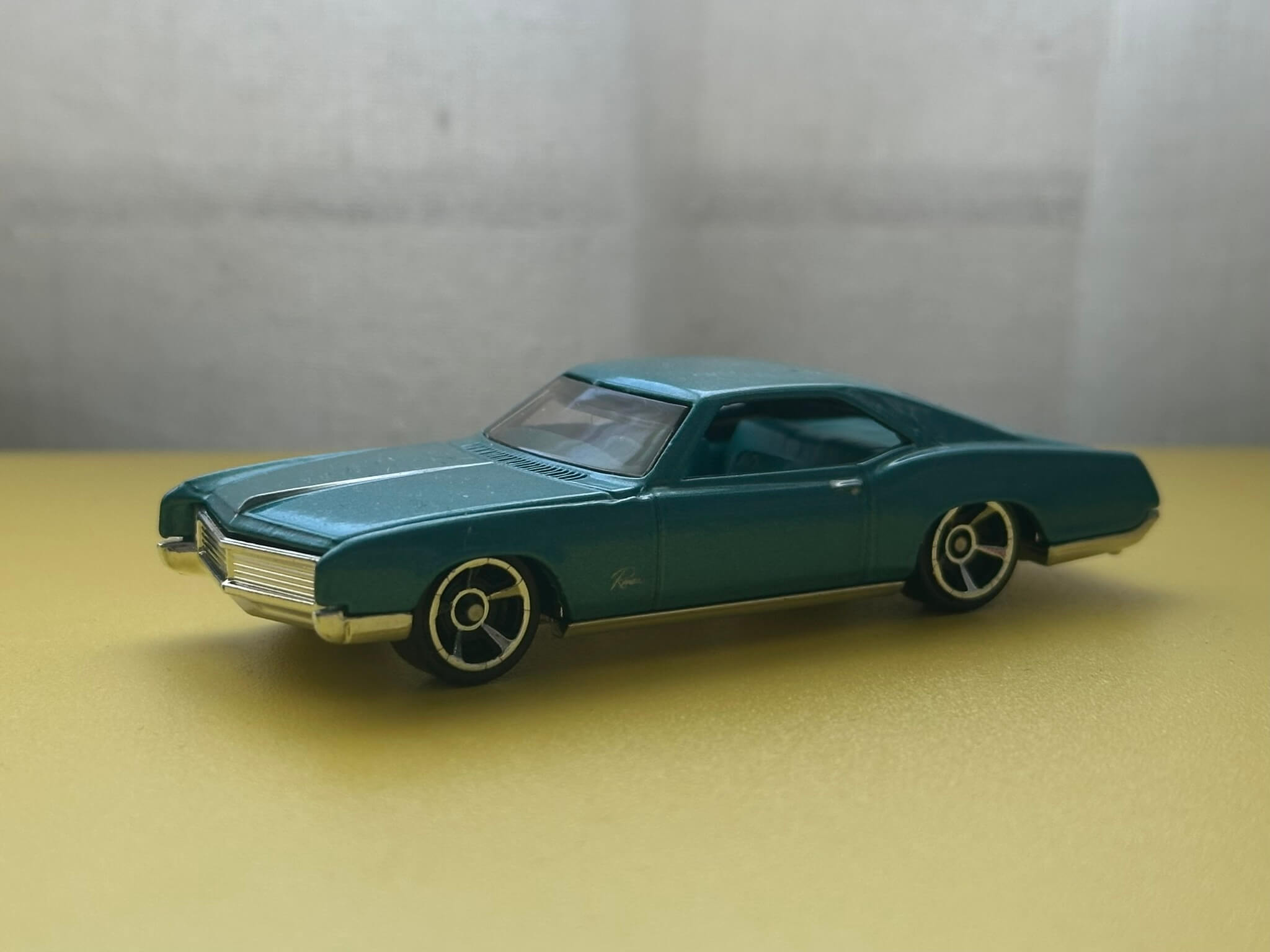 Blue-green toy car sitting on a bright yellow surface