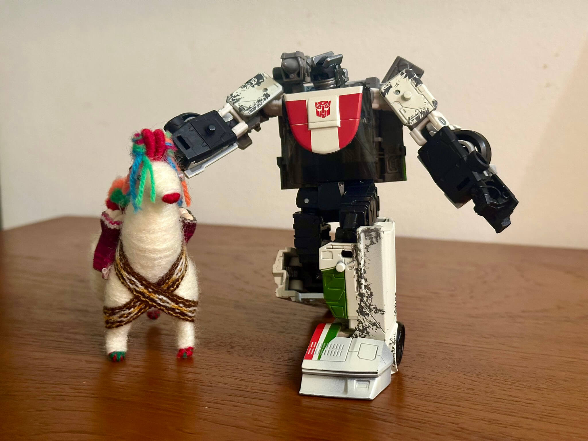 White Transformer crouching down to pat a small toy alpaca