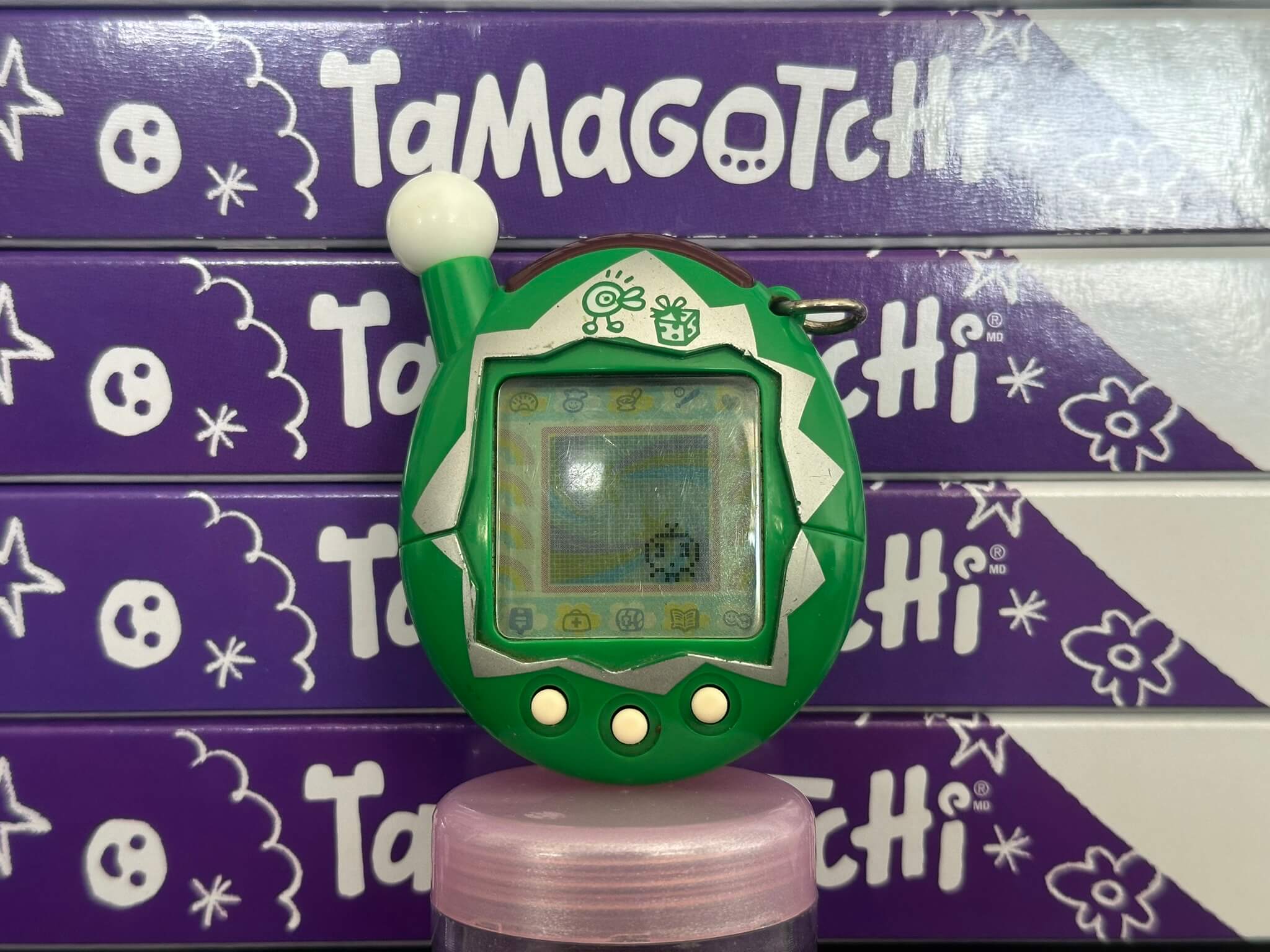 Green Tamagotchi on a background of stacked Tamagotchi boxes