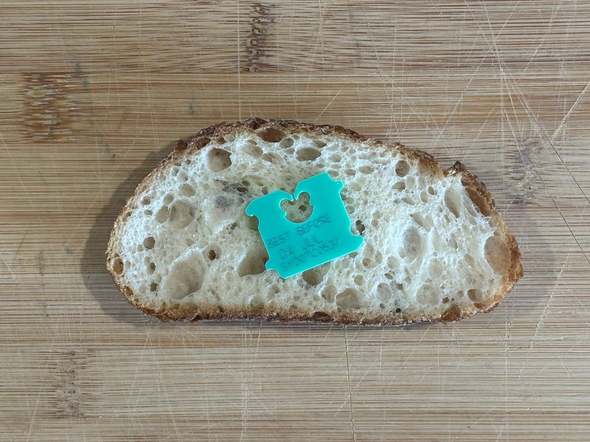 Green bread tag lying on a piece of bread, on a cutting board