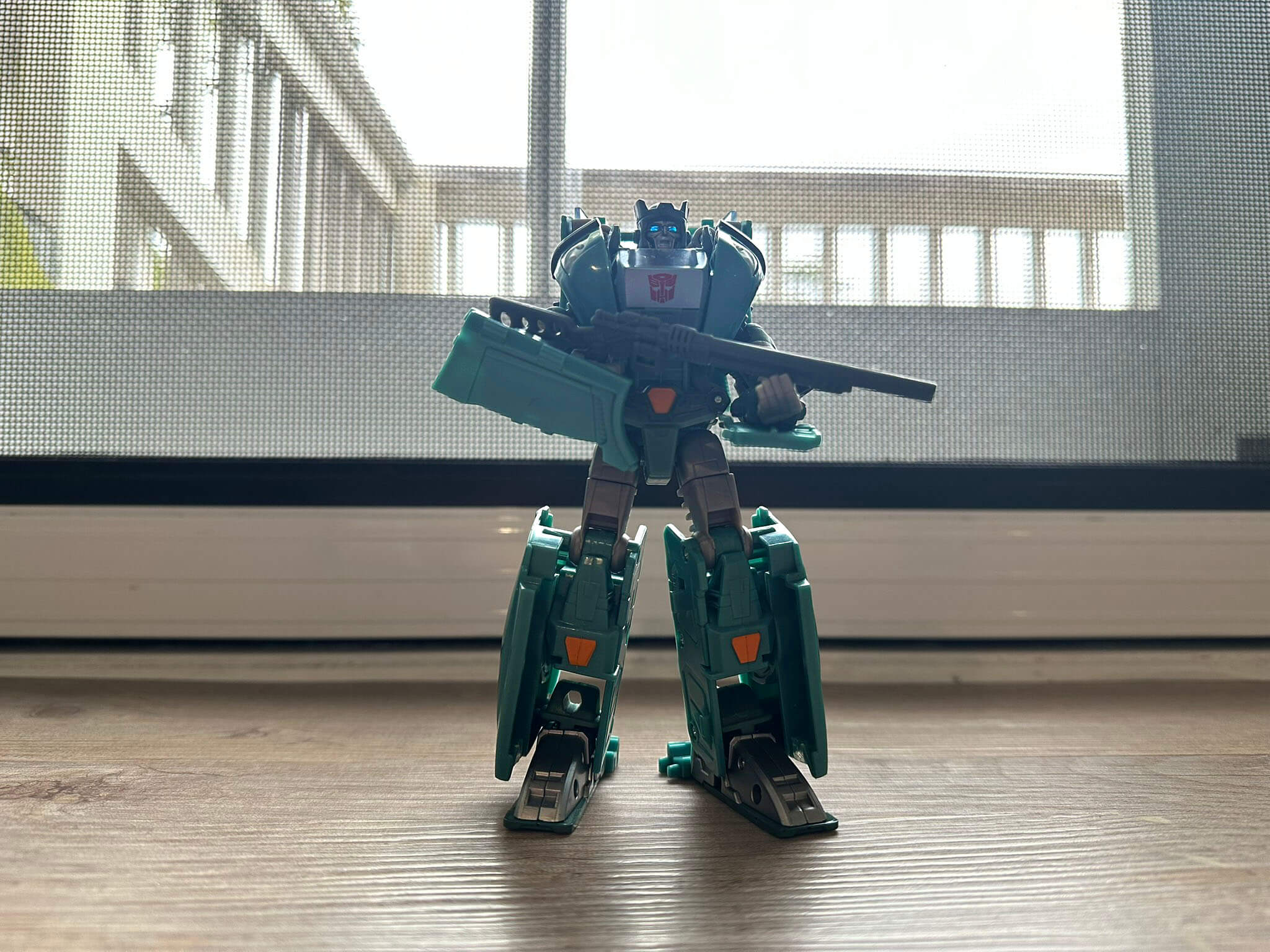 Light green Transformer stood posed with gun in front of screen door